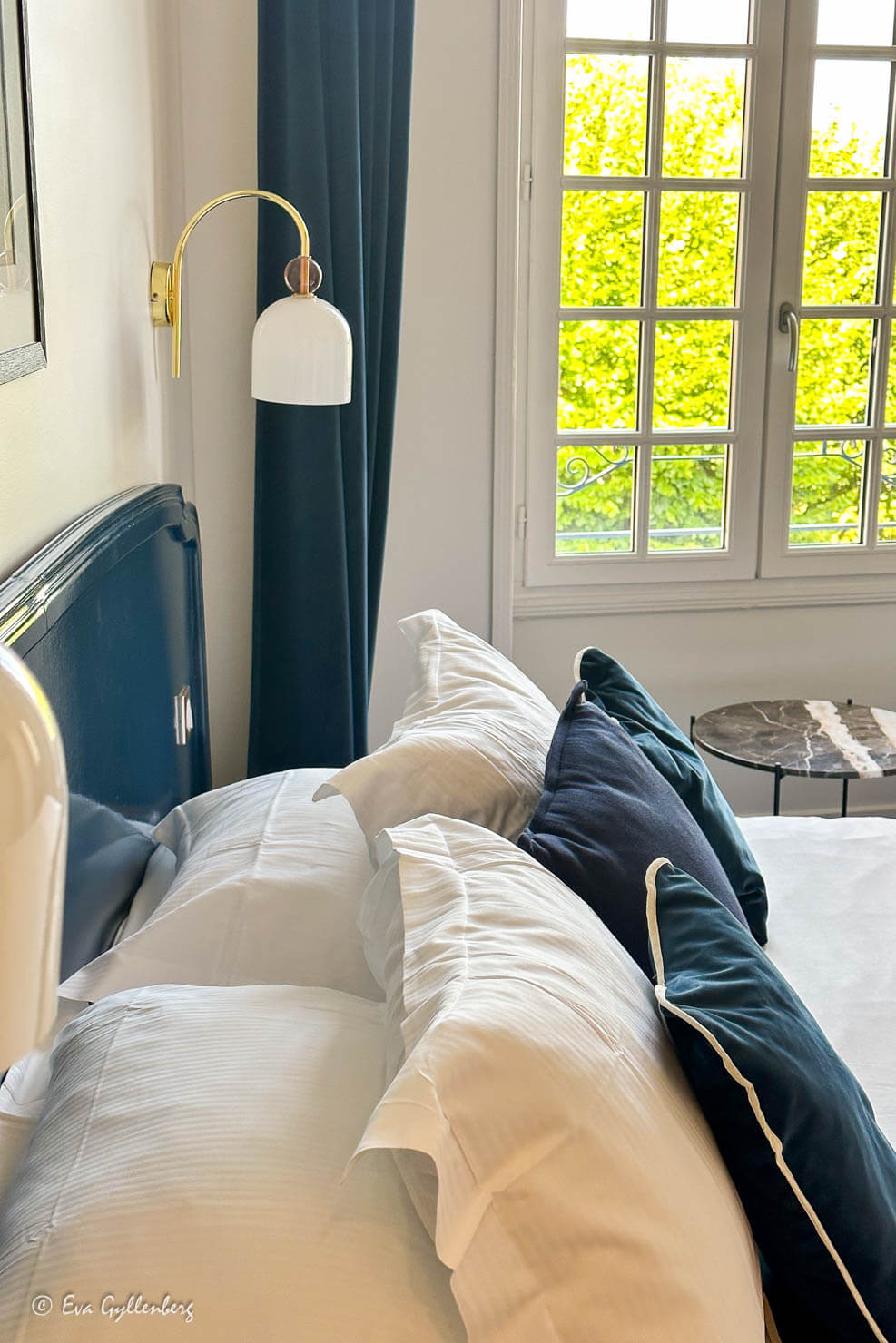 Säng med vita sänglampor och fluffiga kuddar framför ett fönster