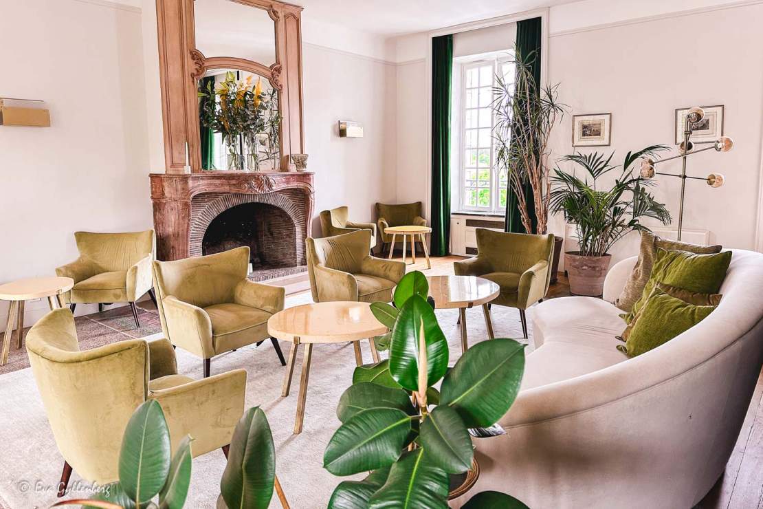 Lounge med sammetsmöbler i beige och grönt och en öppen spis