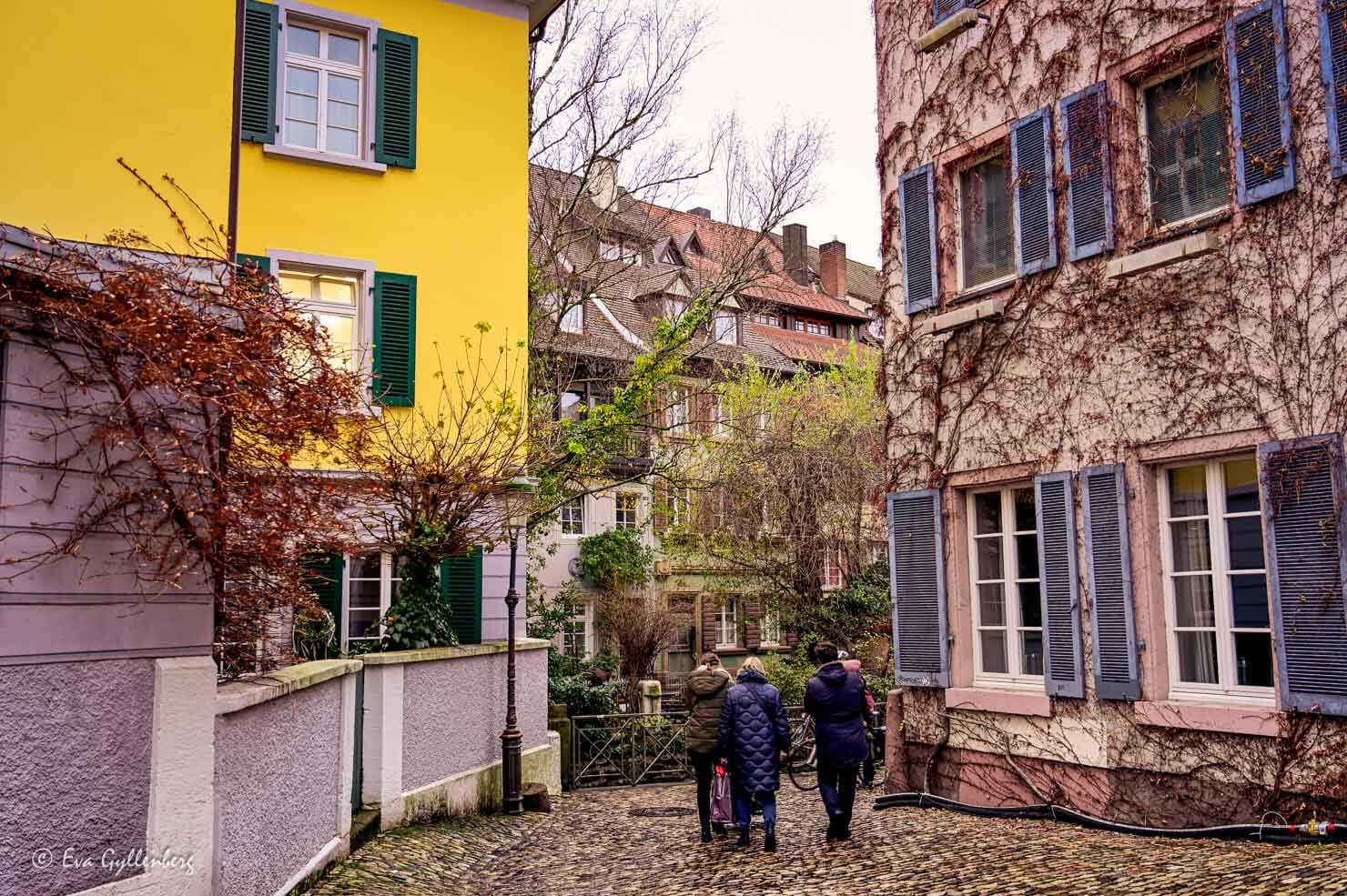 Kullerstensgata mellan två hus med människor som går på gatan