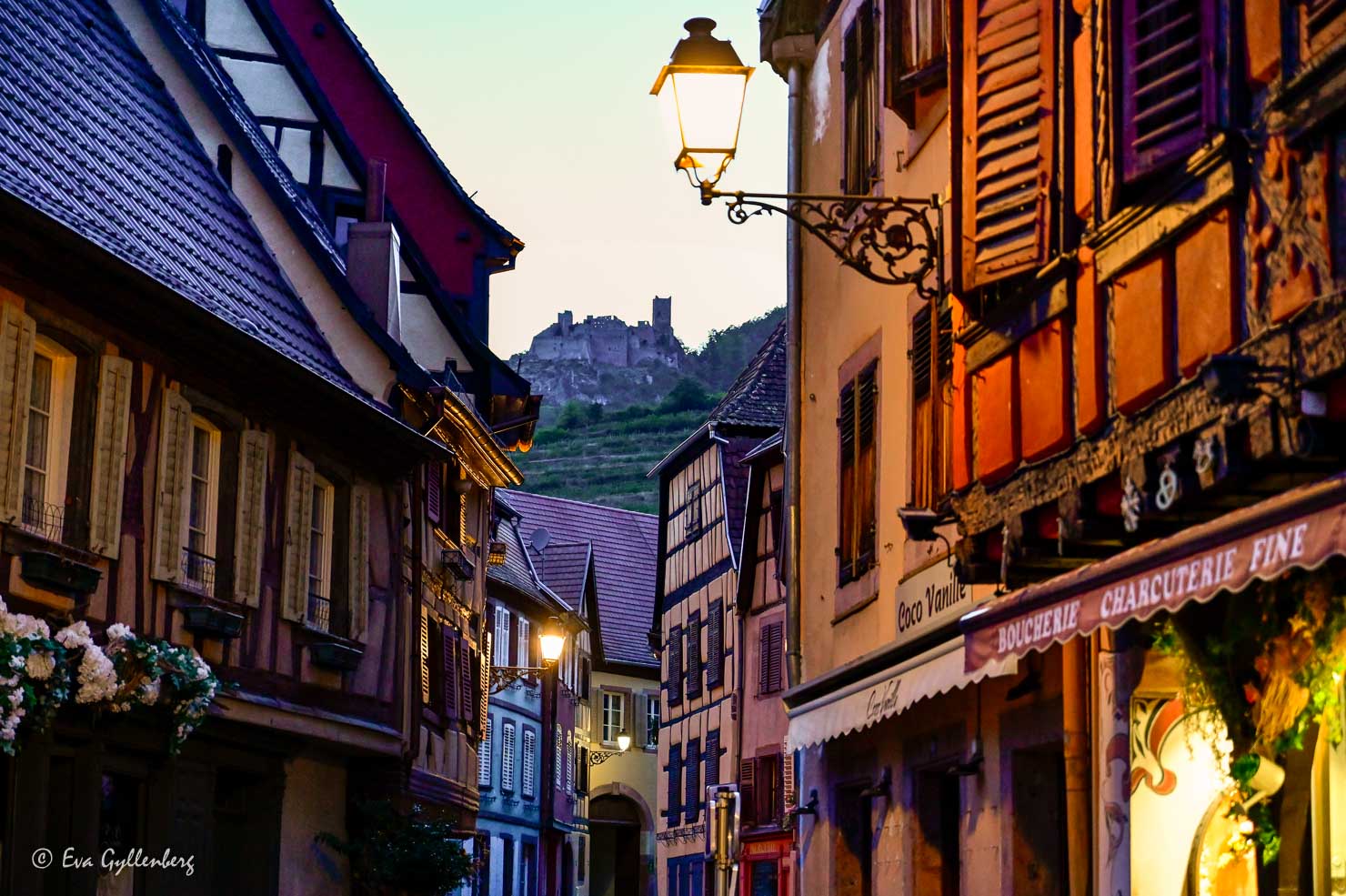 Vacker gata i Alsace med korsvirkeshus och ett slott i bakgrunden på en kulle