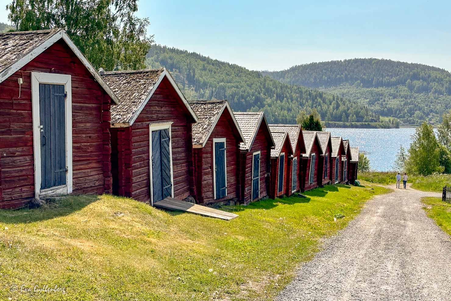 röda kyrkstallar på rad ner mot havet och två människor på promenad