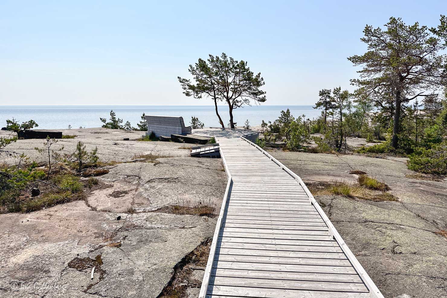 en träspång ut till en träbänk på klippor vid havet