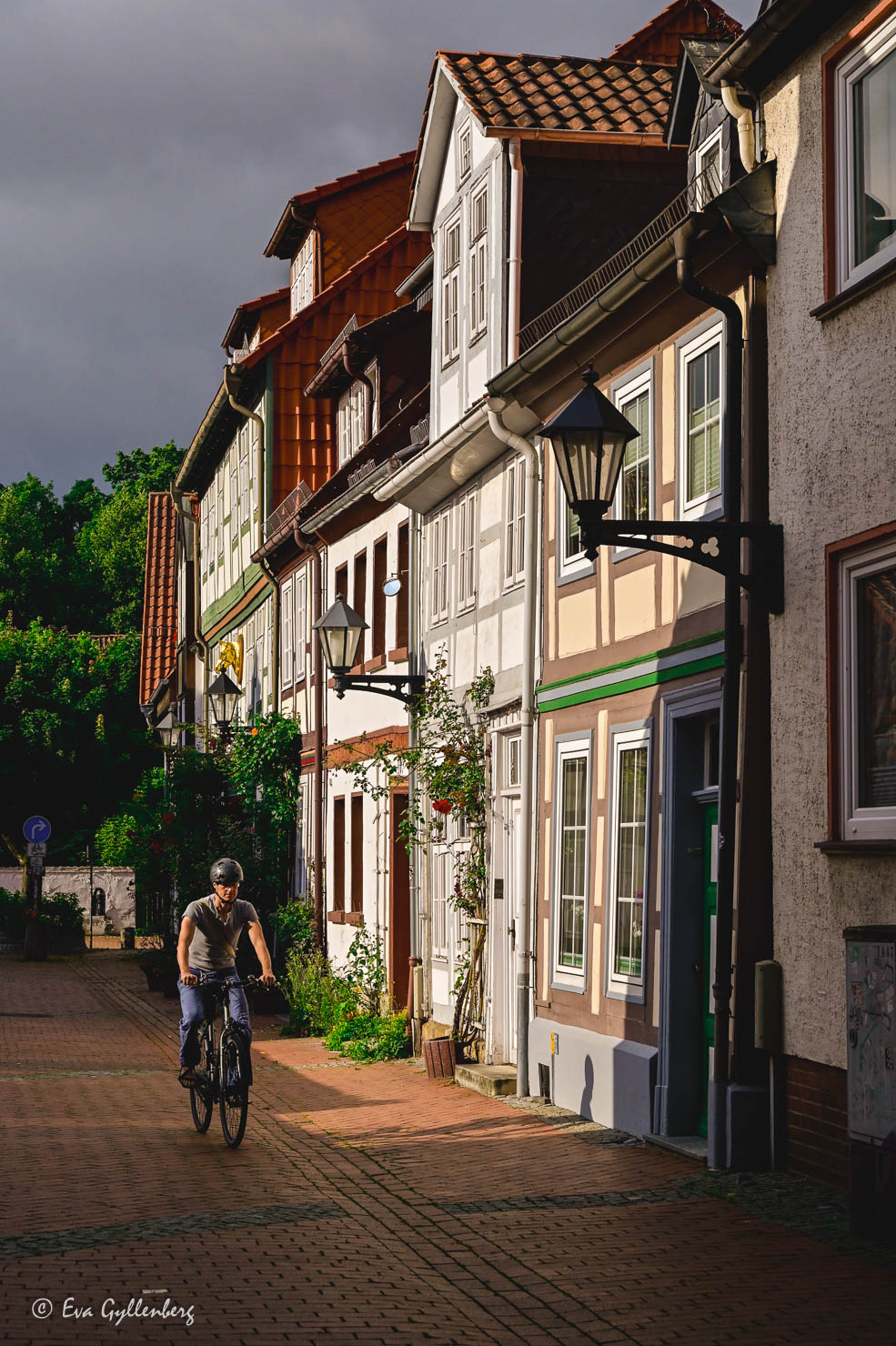 Cyklist i solsken under en mörk himmel på en gata med korsvirkeshus