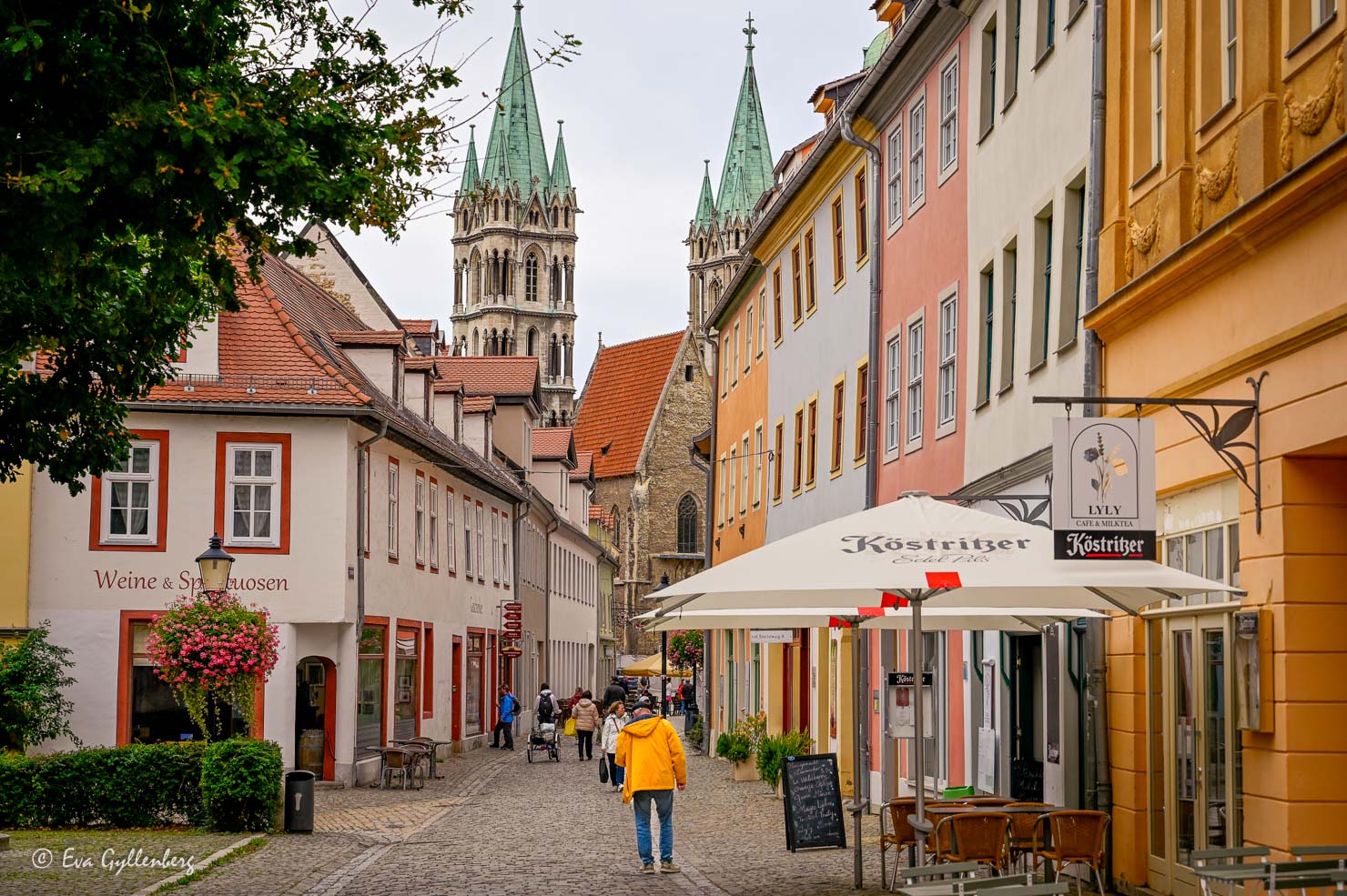 En kullerstensgata med pastellfärgade stenhus och en katedral i horisonten