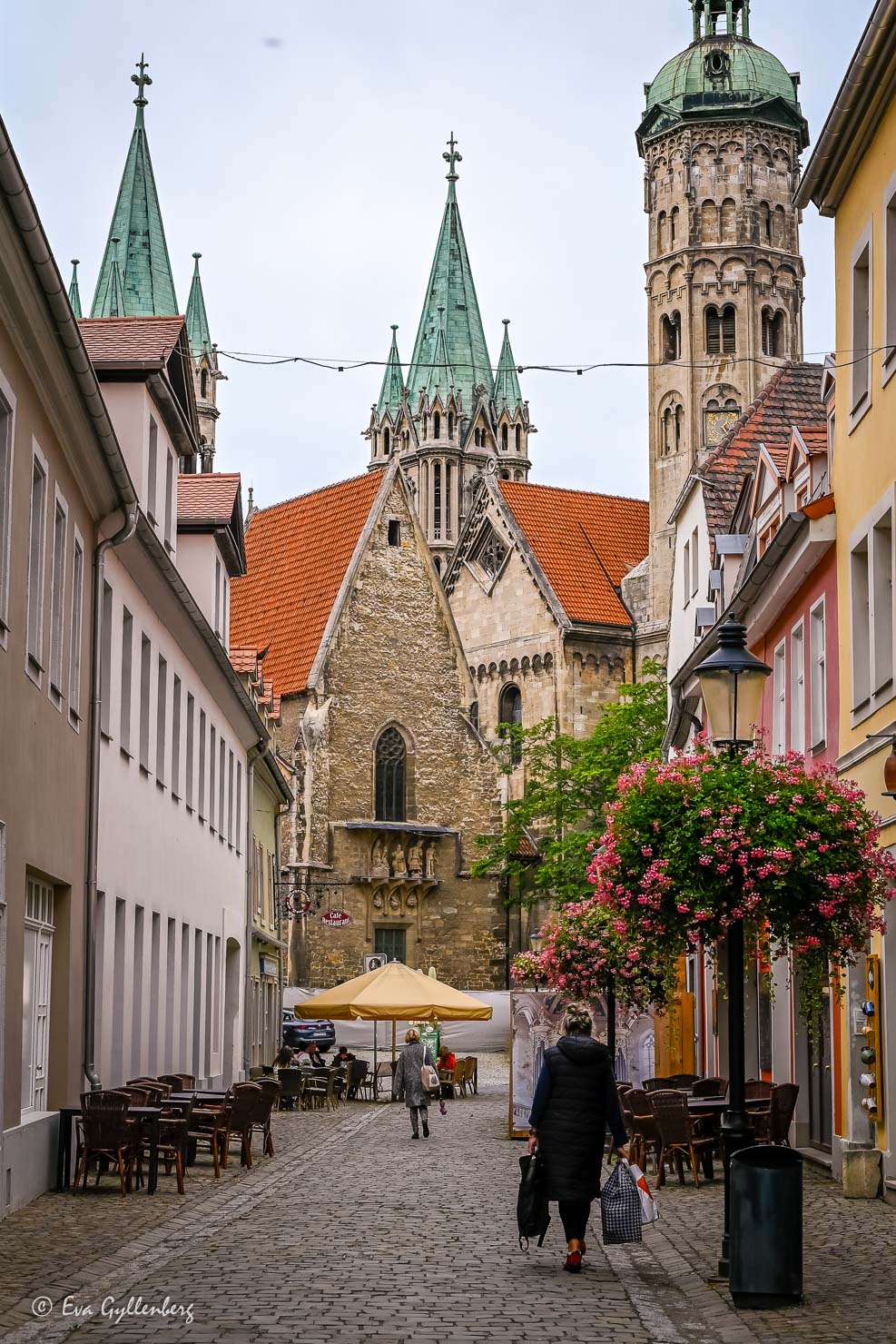 En kvinna går på en kullerstensgata med pastellfärgade stenhus och en katedral i horisonten