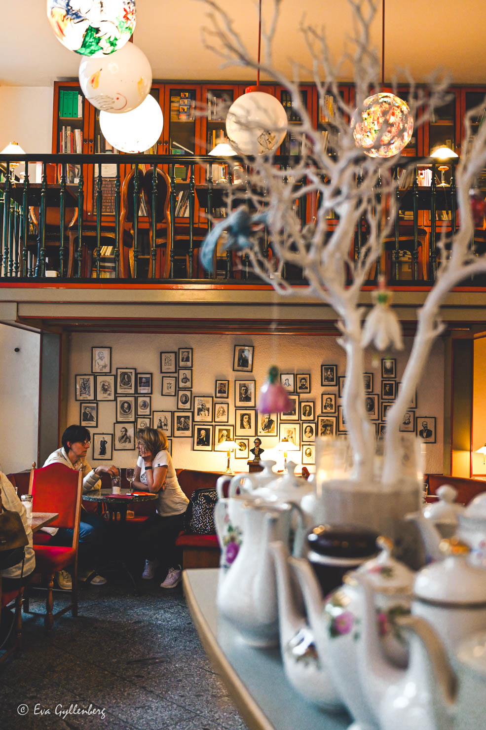 café med gäster i två våningar med runda lampor i taket och många tavlor på väggen