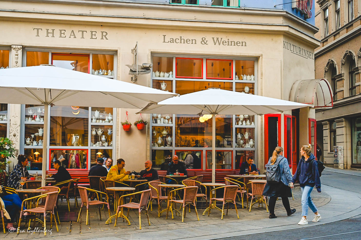 uteservering med möbler och parasoller framför ett vackert hus med kaffekannor i fönstren