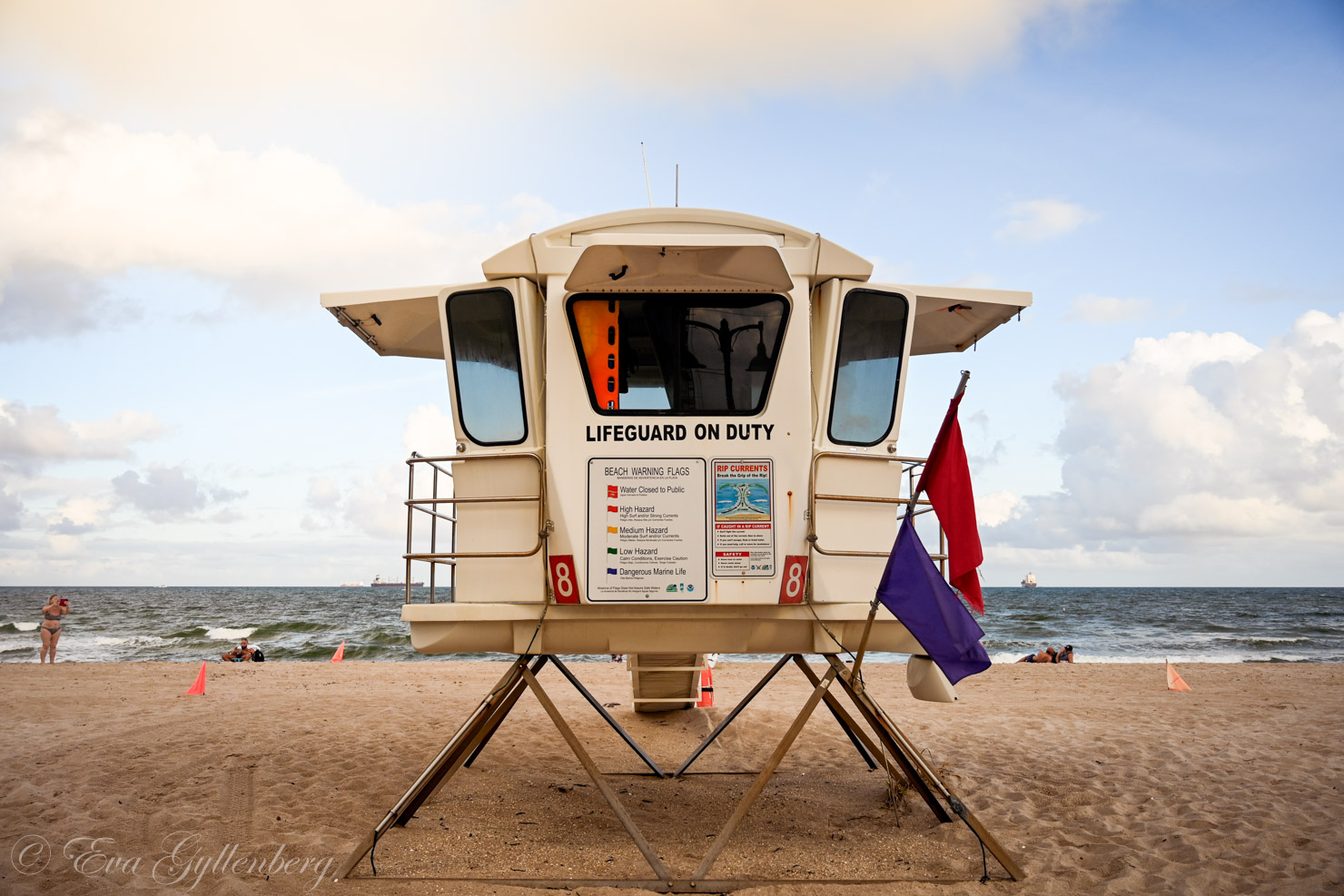 ett öppet livräddartorn med flaggor på en strand med badare