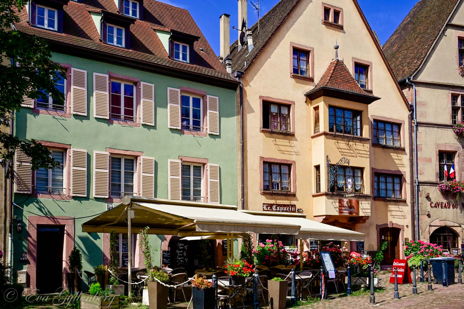 Ett mintgrönt och ett ljusgult hus på ett torg i Alsace